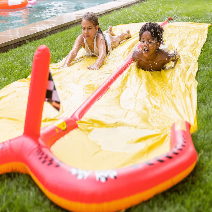 Kids racing on an inflatable water slide with double tracks in a backyard, enjoying a sunny summer day.