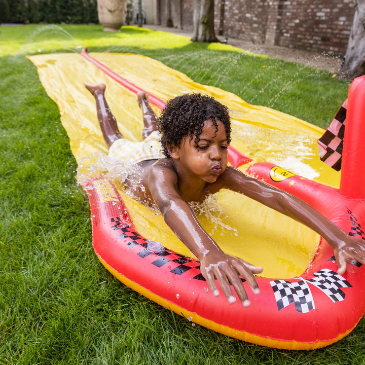  Kids racing on an inflatable water slide with double tracks in a backyard