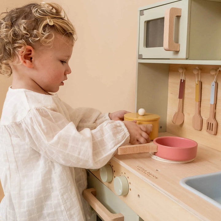 Toddler playing with wooden play kitchen accessories