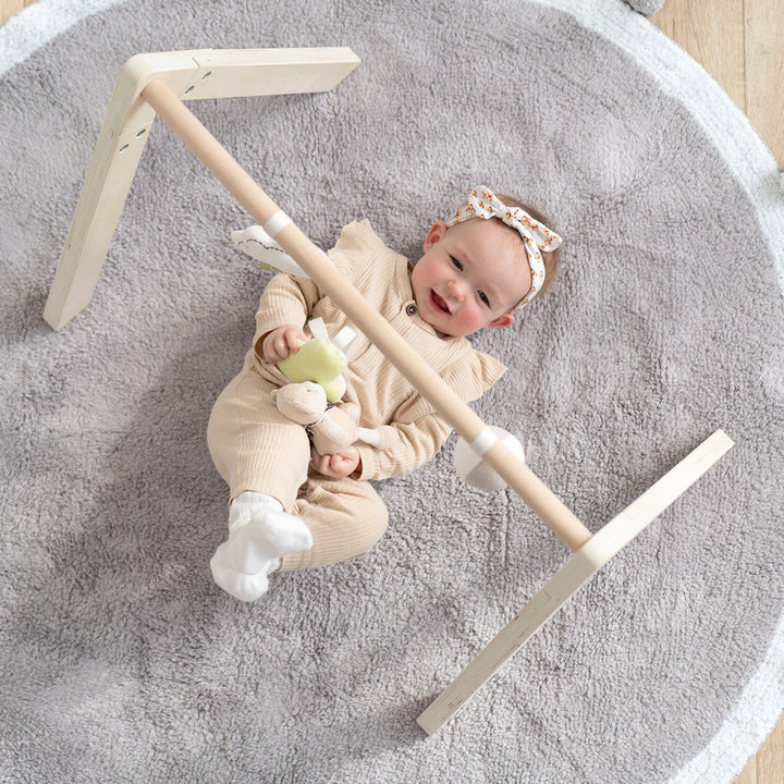 A happy baby is playing with the wooden baby gym set: Moon and Star Adventure.