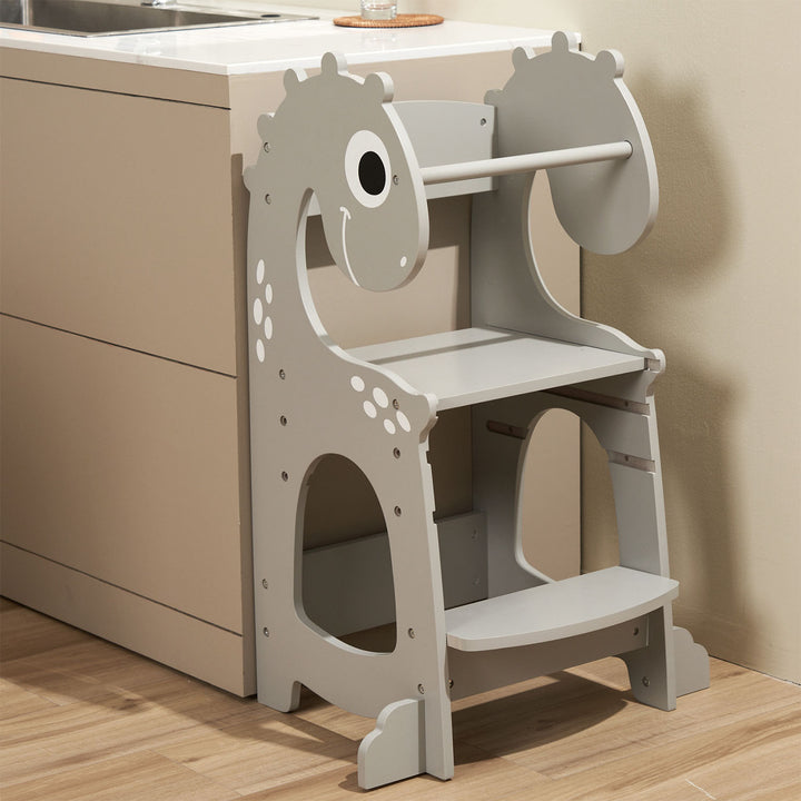 The Dino Grey toddler tower placed next to a kitchen counter, showcasing its compact and stylish design, perfect for encouraging toddler involvement in cooking.