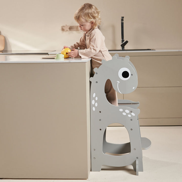 Toddler standing on the Dino learning tower at counter height, safely engaged in kitchen activities.