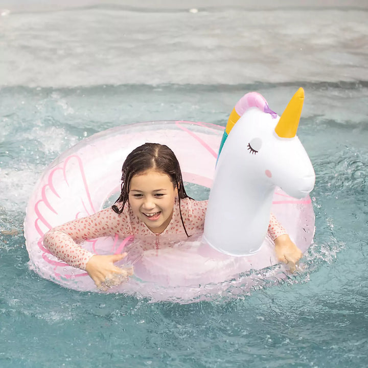 Child floating joyfully on a magical unicorn swim ring with rainbow mane and wings.