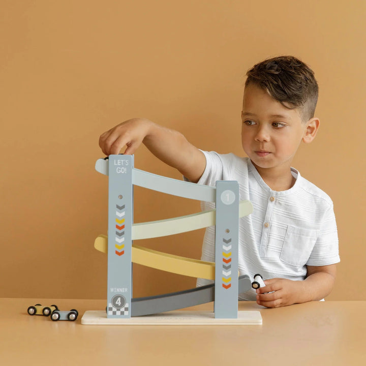 A child playfully racing four colorful wooden toy down a blue painted wooden ramp.