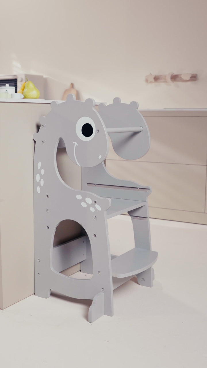 Video of Dino Grey toddler tower in use, showing child safely climbing to kitchen counter height. Features adjustable height, anti-slip steps, rounded edges, and dinosaur design, fostering independence and safe kitchen involvement for toddlers.