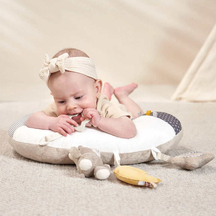 A sweet baby is playing with a tummy time pillow, a teether, and a plush bunny.